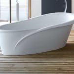Freestanding white acrylic bathtub with curved design on wooden floor