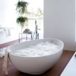 Freestanding oval white bathtub with foam on wooden floor