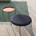 Round fabric pouf with metal legs beside small round tray table