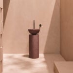 Round resin washbasin on cylindrical pedestal in bathroom setting