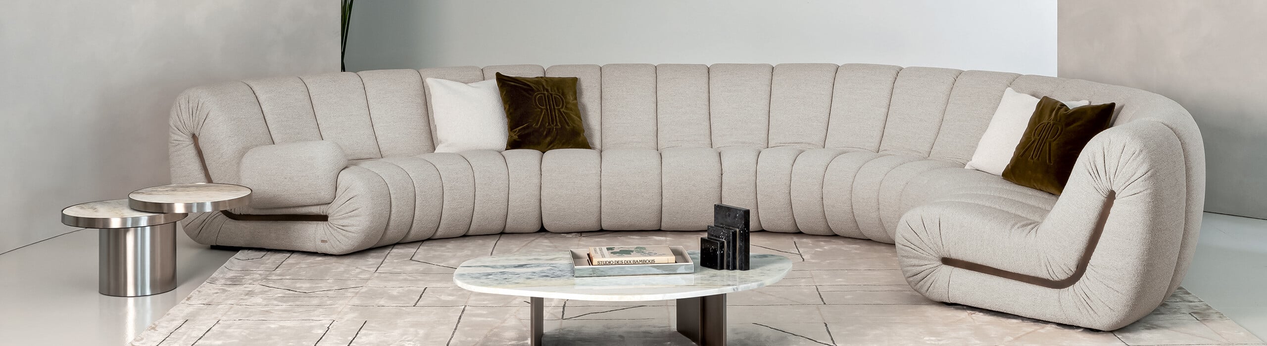 Beige fabric curved sectional sofa with cushions beside round marble coffee tables
